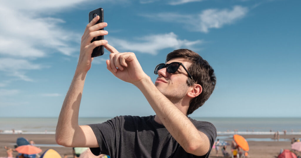 Young man on the coast looking for signal on his smart phone. Concept of connectivity and connection problems.
