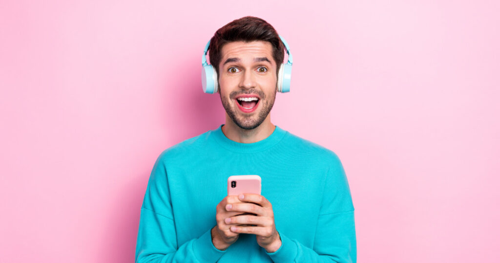 Budget headphones on man in teal sweater holding smartphone