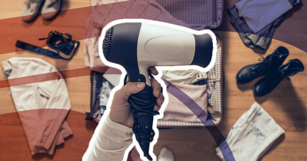 hair dryer being held above a suitcase, with items to be packed scattered around