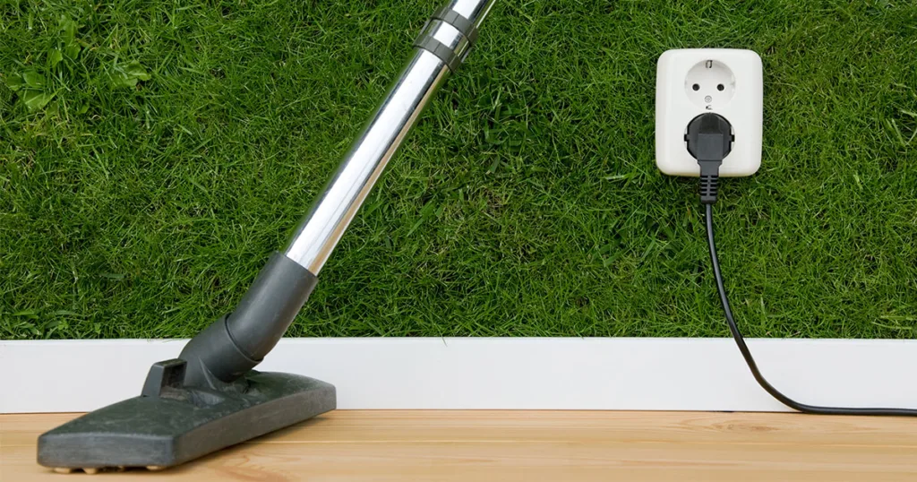 plug and cord plugged into a greeb, grass wall. A vacuum head and shaft leans against the wall next to it