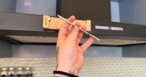 Meater Pro prob held in a hand with the wooden box stuck on a matte black rangehood in the background