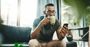 Man drinking from mug while reviewing phone screen