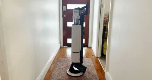 Samsung Jet AI Ultra in white standing in the middle of a white hallway, on an orange patterned rug
