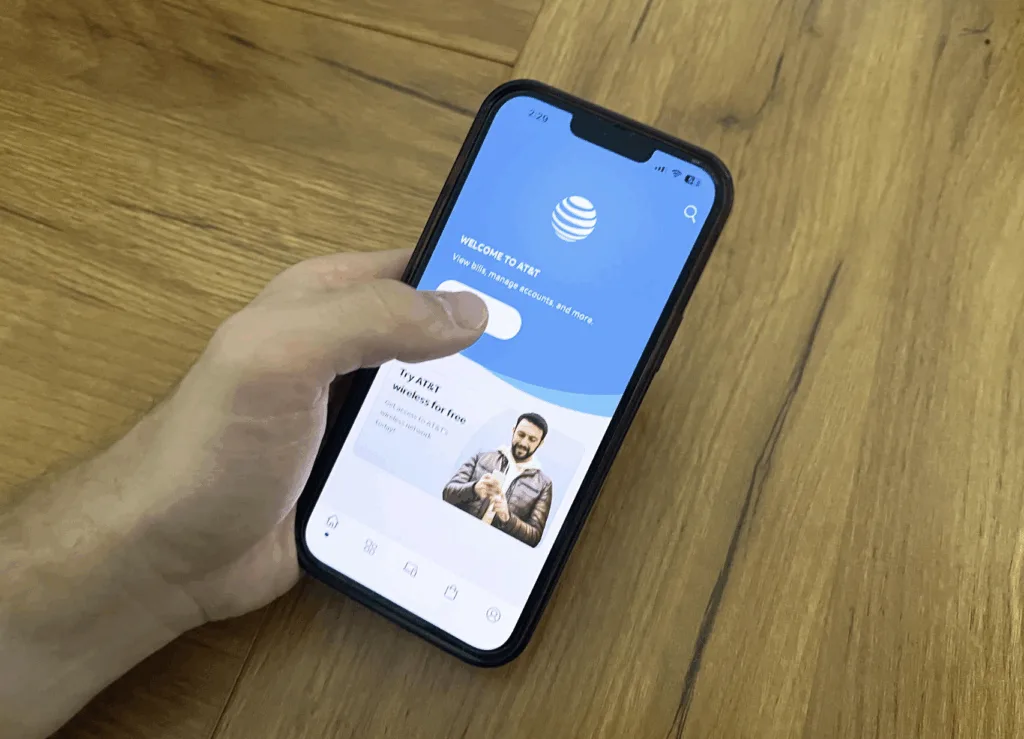 A person holds a smartphone displaying the AT&T app home screen.