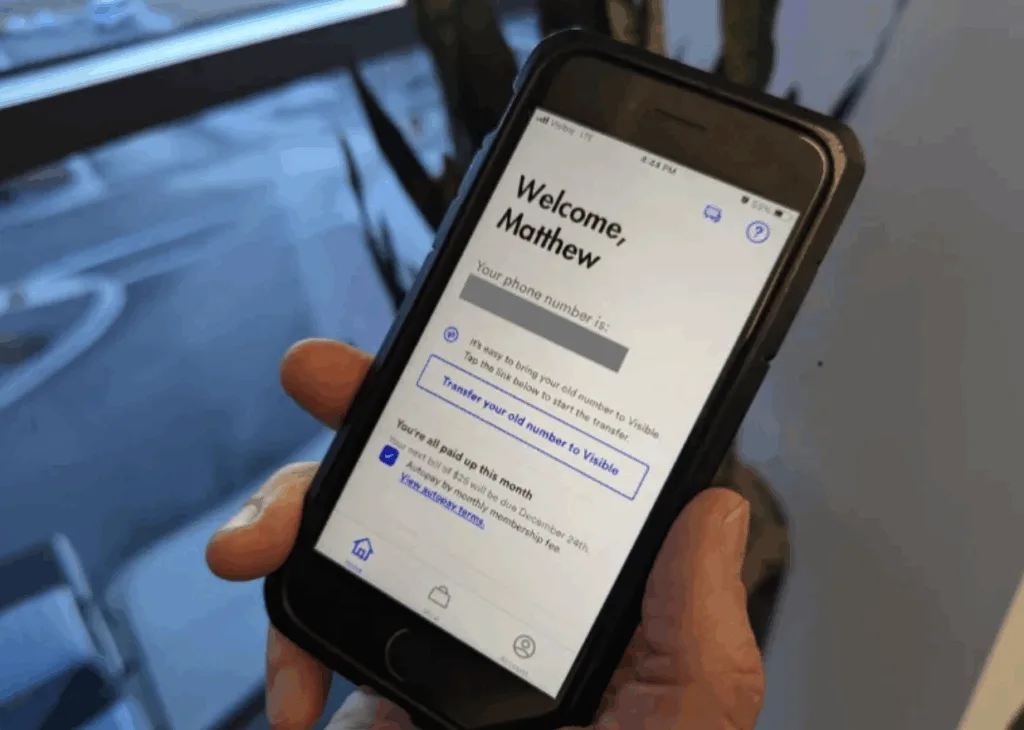 A person holds a smartphone displaying the Visible wireless onboarding screen