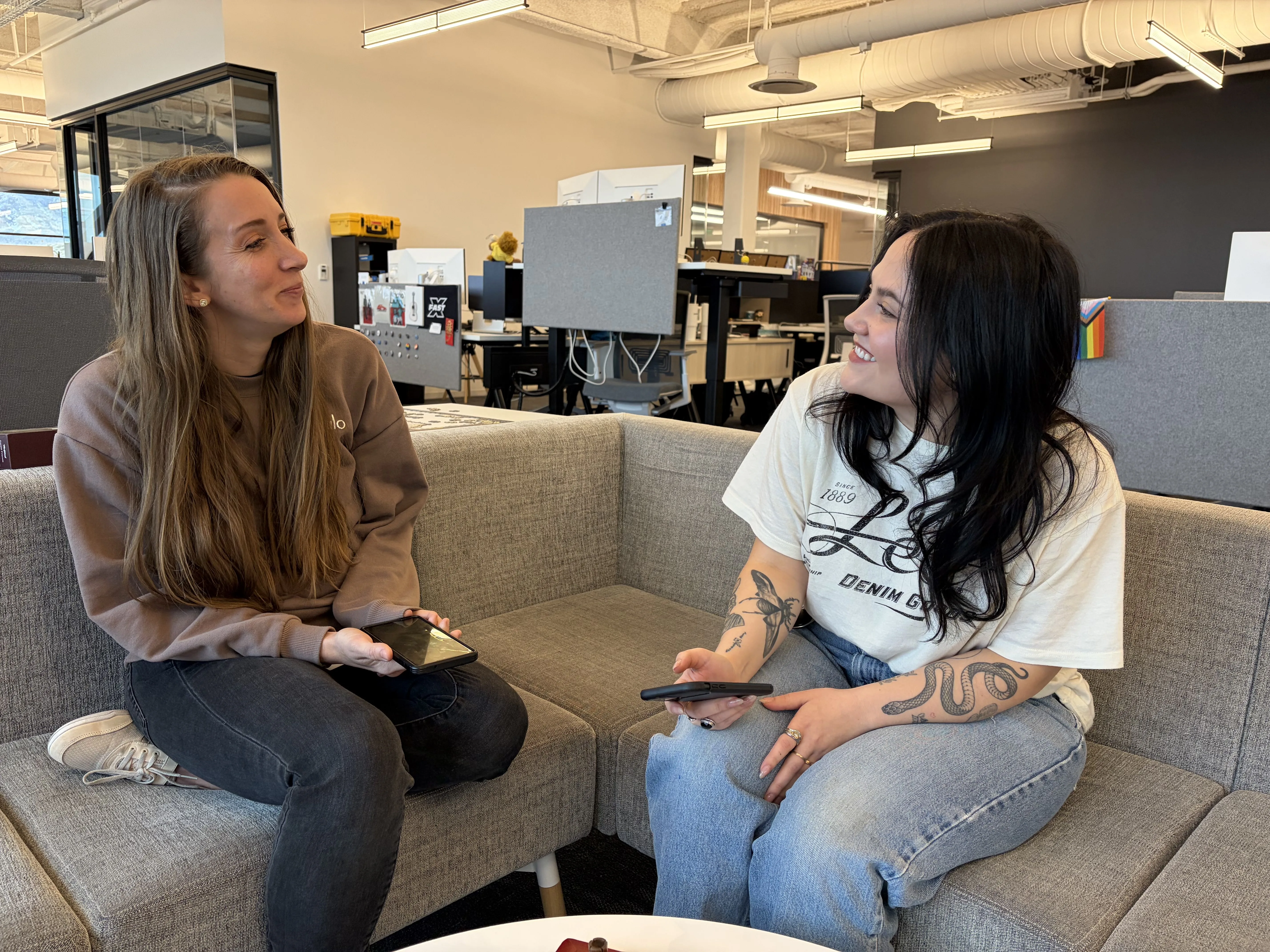 Two ladies sit side by side on a couch, holding phones and discussing mobile coverage.