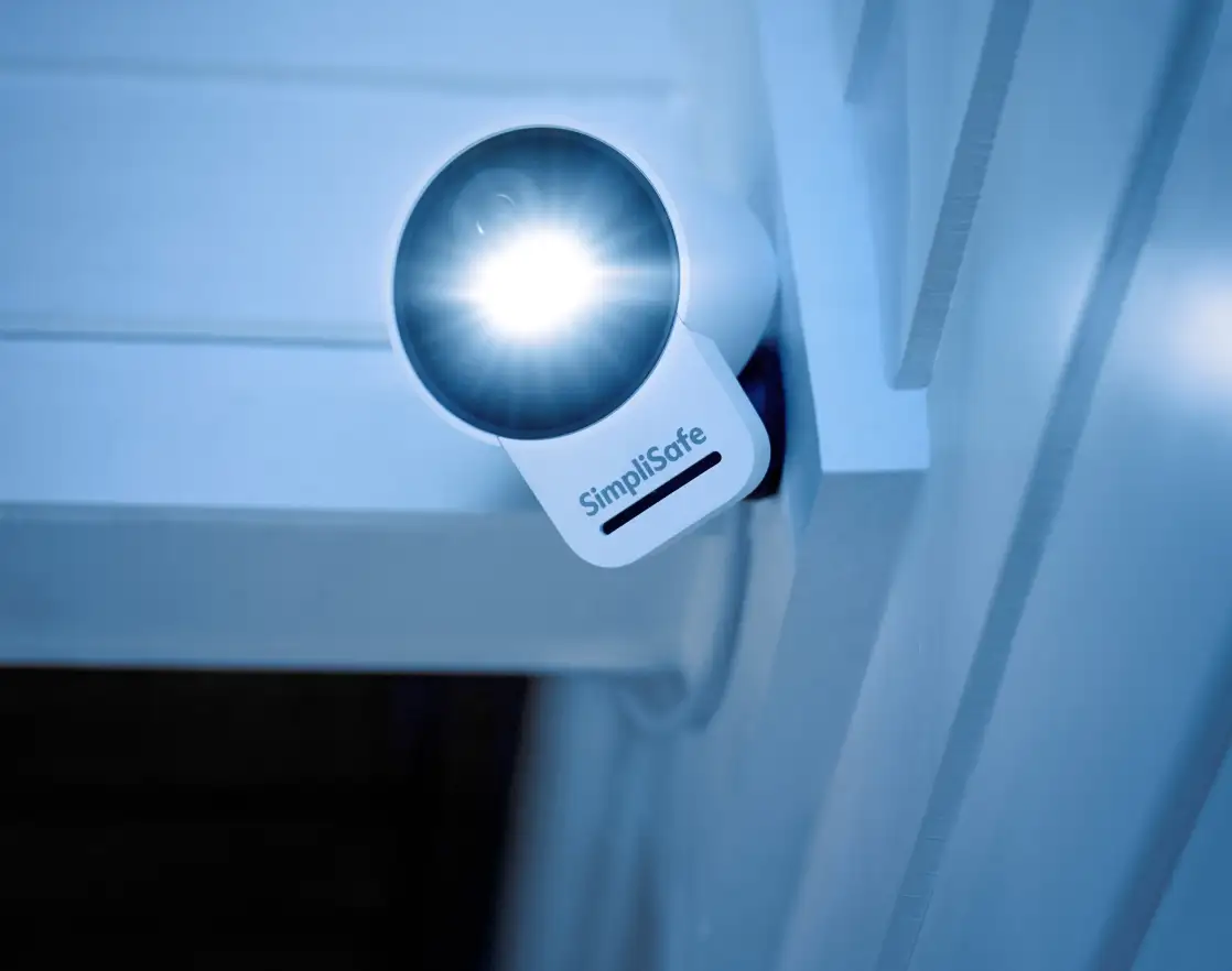 SimpliSafe Outdoor Camera Series 2 mounted on a home exterior and shining brightly at night