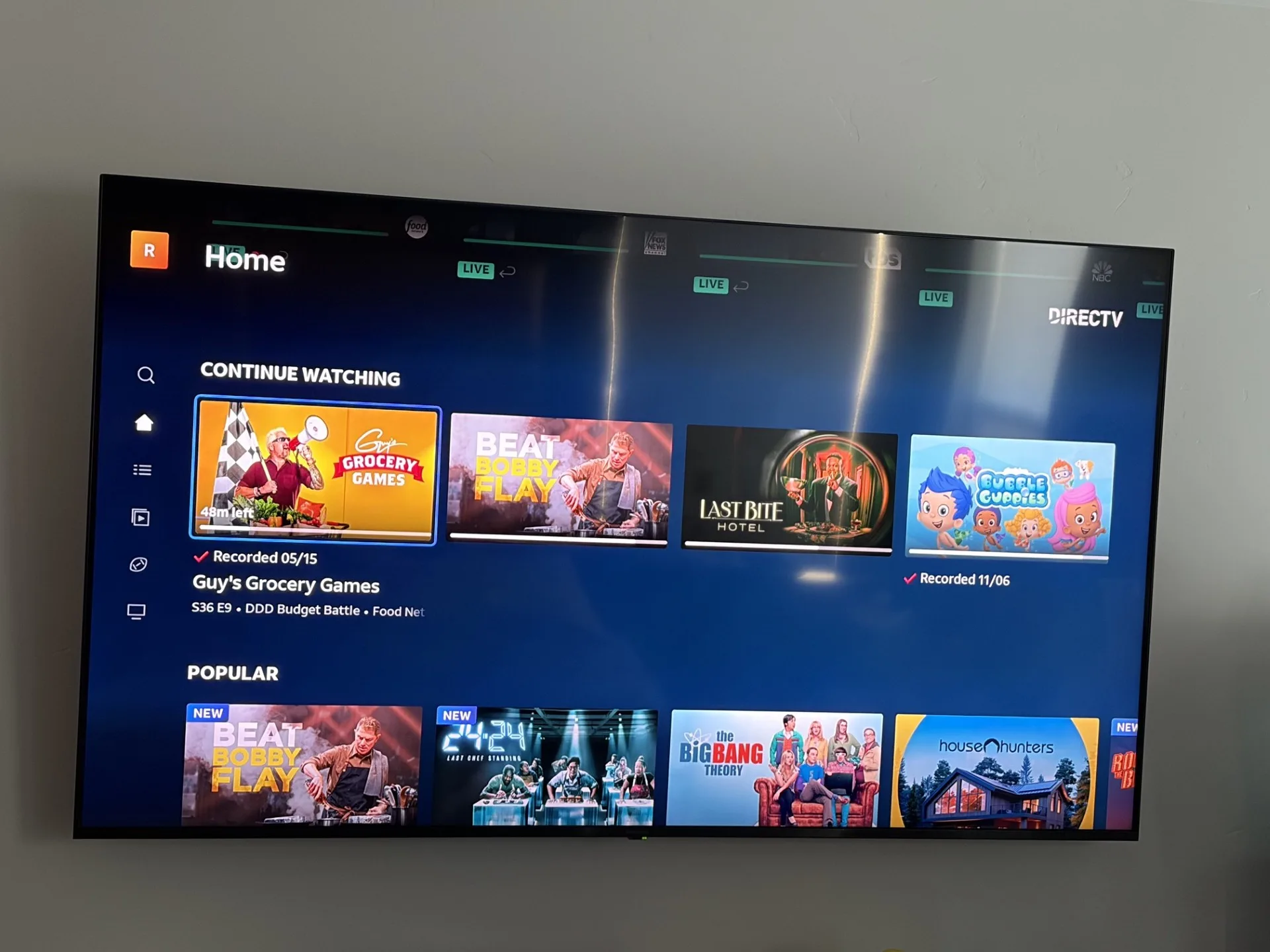 TV screen showing the DIRECTV streaming app home screen, including shows in progress and popular options