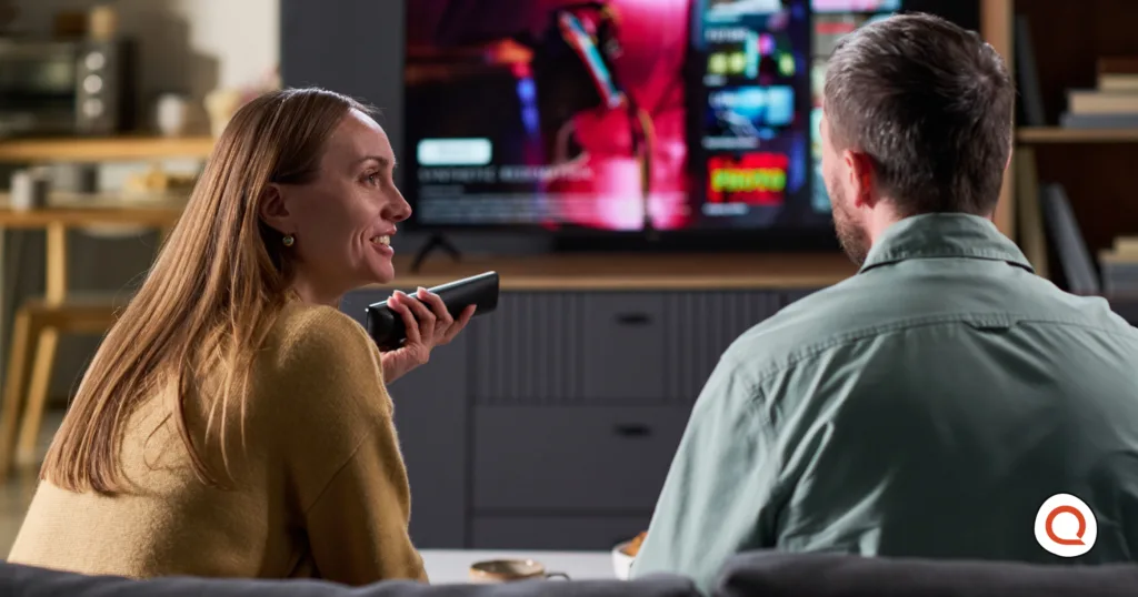 Couple sitting on a couch browsing a streaming service on their TV using a voice remote control