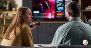 Couple sitting on a couch browsing a streaming service on their TV using a voice remote control