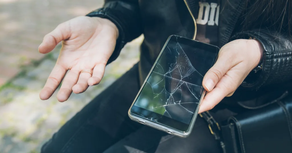 Woman holding a cracked smartphone with a shattered screen in her hands outdoors