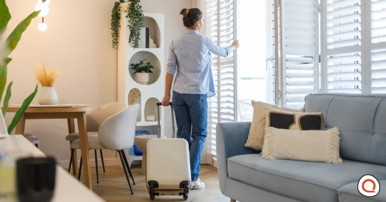 Person preparing to leave home with suitcase while checking window blinds before travel for home security