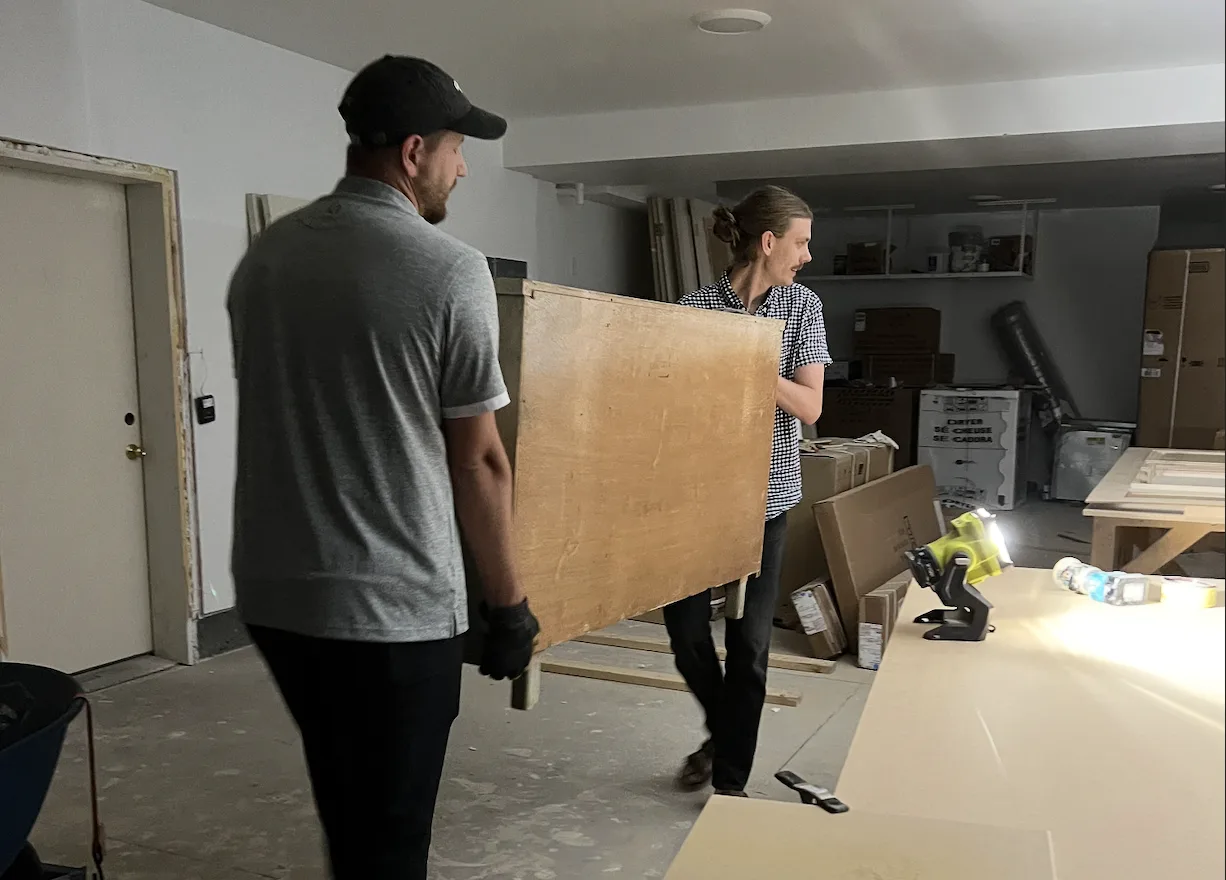 Two men carry a chest of drawers into a garage as a family moves into their home.