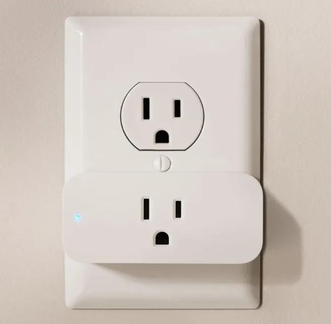 Amazon Smart Plug inserted into the bottom outlet of a standard wall outlet, with a status light visible on the side.