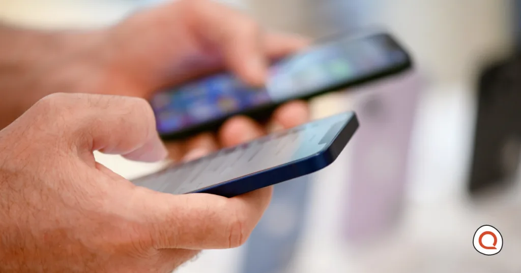 A shopper holds and compares two smartphones in a retail store, with more phones on display in the blurred background.