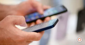 A shopper holds and compares two smartphones in a retail store, with more phones on display in the blurred background.