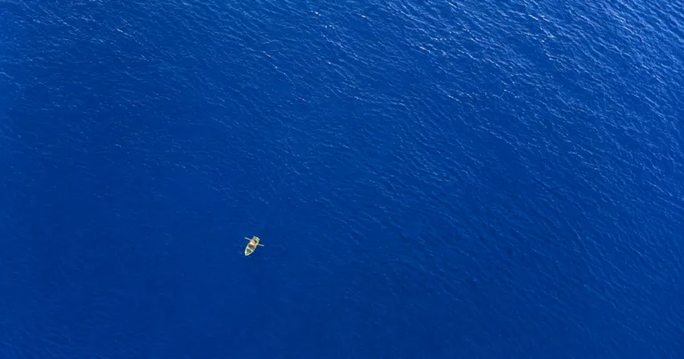 Aerial view of a person rowing a small boat alone across a vast stretch of open water.