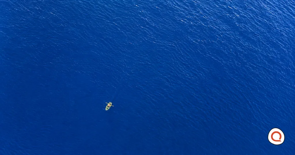 Aerial view of a person rowing a small boat alone across a vast stretch of open water.