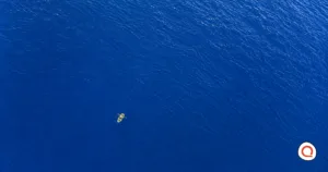 Aerial view of a person rowing a small boat alone across a vast stretch of open water.