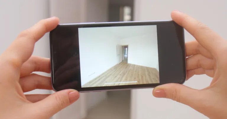 A person holds up an iPhone, using its camera to scan an empty room, illustrating how LiDAR helps map physical spaces.