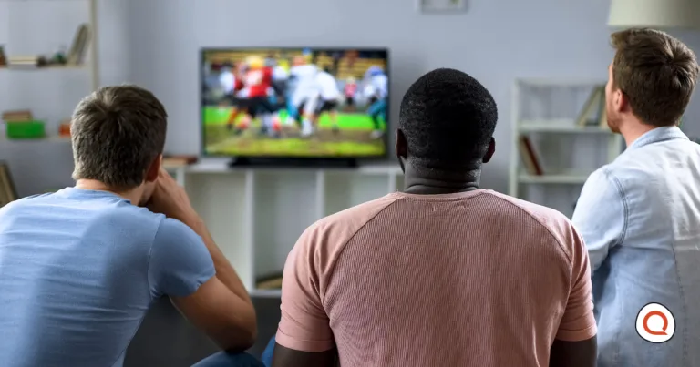 Three friends watch a college football game on TV from a living room couch.