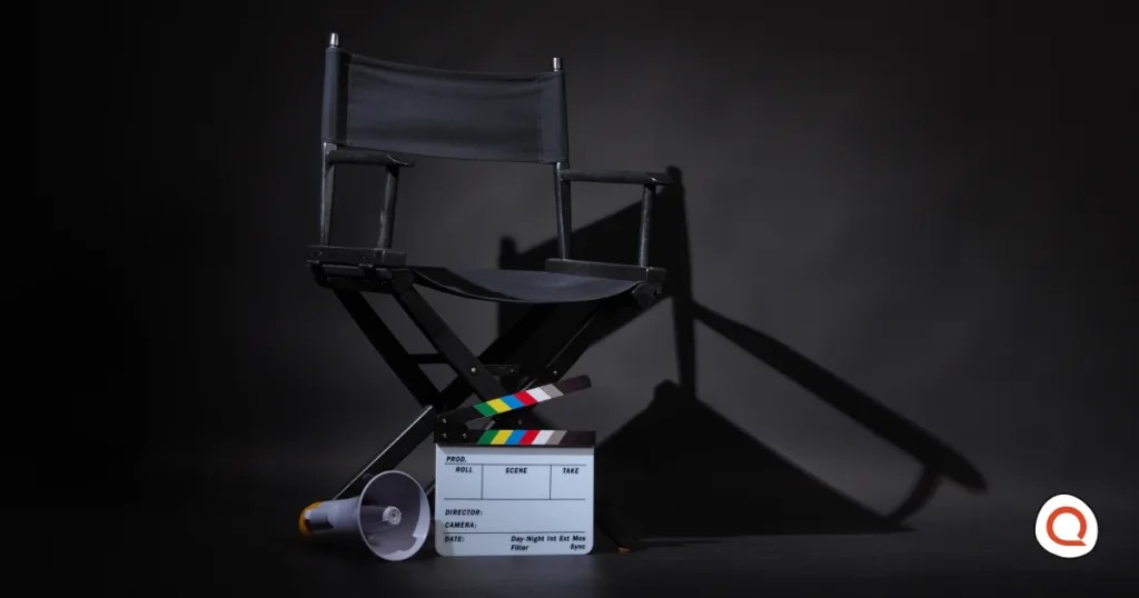 An empty director's chair on a dark soundstage, with a clapperboard and megaphone at its base.