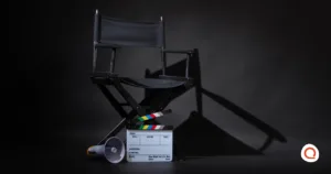 An empty director's chair on a dark soundstage, with a clapperboard and megaphone at its base.