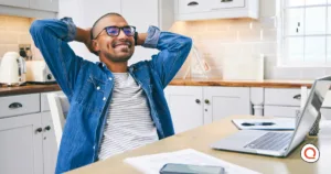 Man relaxing at his kitchen table with a laptop and phone, representing peace of mind that comes with reliable backup internet at home.