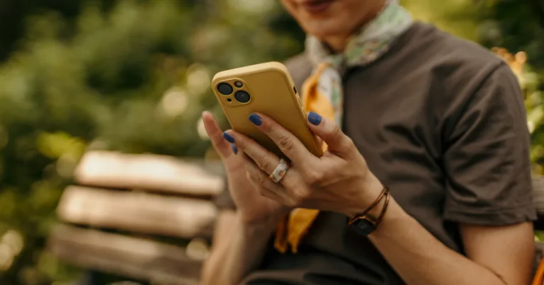 A woman checking her phone outdoors, holding on to her current device rather than rushing to upgrade to the newest model.