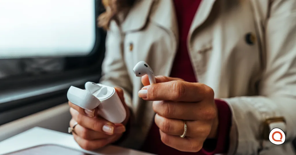 A woman holding true wireless earbuds and their charging case while commuting, reflecting on the buying advice from a long-term owner.