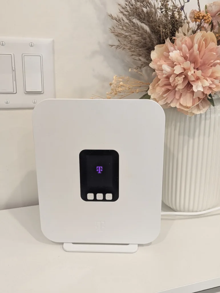 T-Mobile 5G Home Internet gateway device on a desk with a floral arrangement behind it