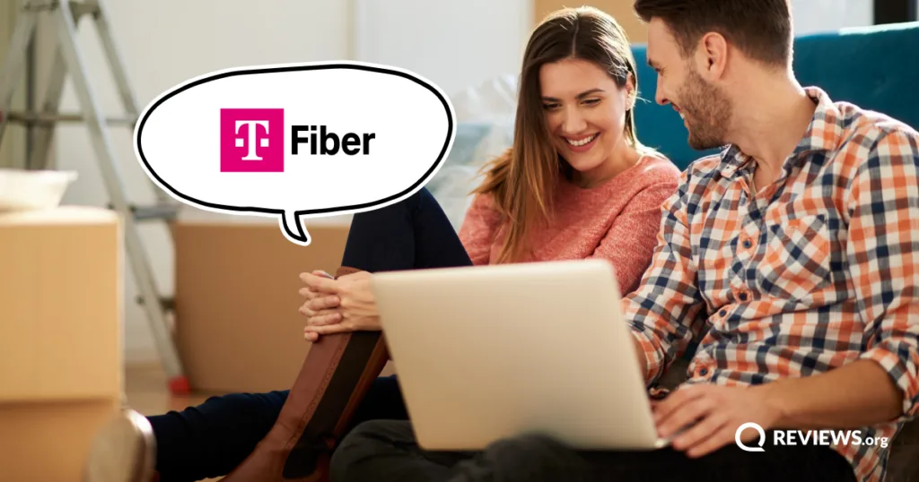 A couple sits on the floor amid moving boxes, looking at a laptop together, with a T-Mobile Fiber speech bubble beside them.