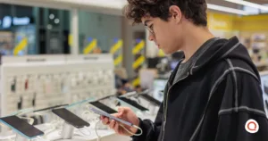 Young teenager examining a smartphone at a mobile phone retail store display, comparing different device options