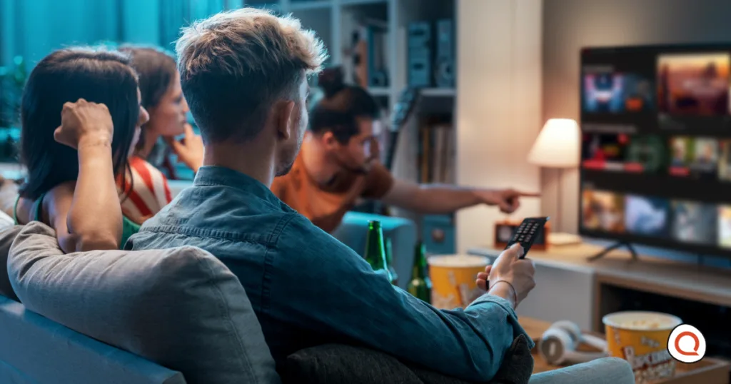 Group of friends gathered on a couch watching streaming content on a television, with snacks and drinks nearby