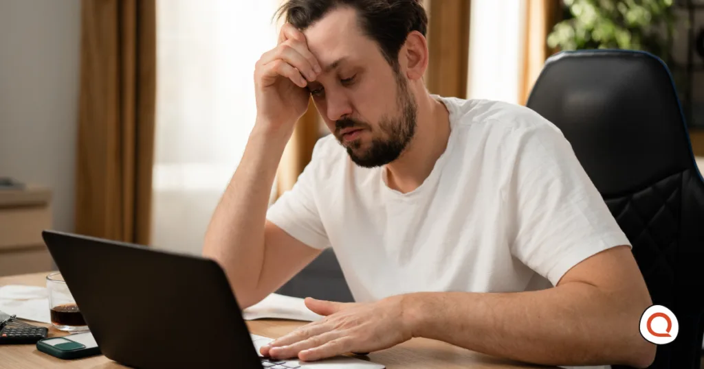 Frustrated man rubbing his forehead while staring at a slow-loading laptop, representing the signs of internet throttling from an ISP.