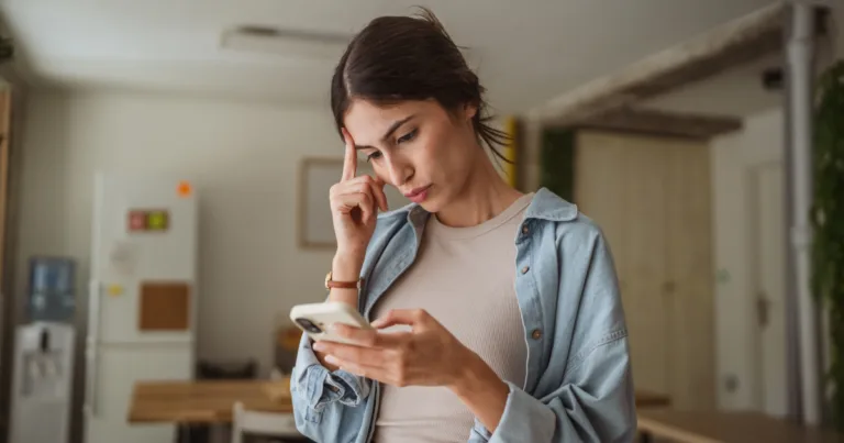 A woman looking concerned while checking her phone, wondering why her "unlimited" data plan has slowed down.