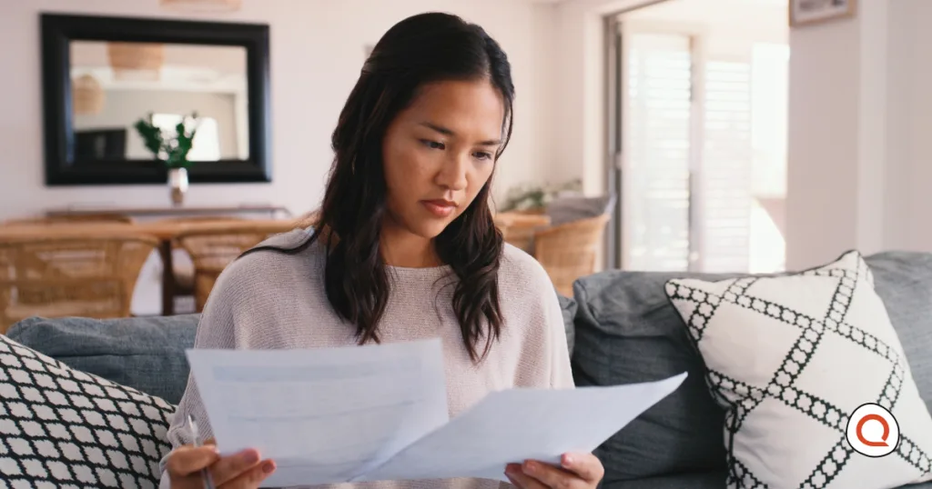 A woman reviews financial paperwork at home, weighing which bills to cut as other costs rise.