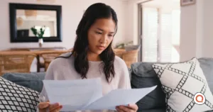 A woman reviews financial paperwork at home, weighing which bills to cut as other costs rise.