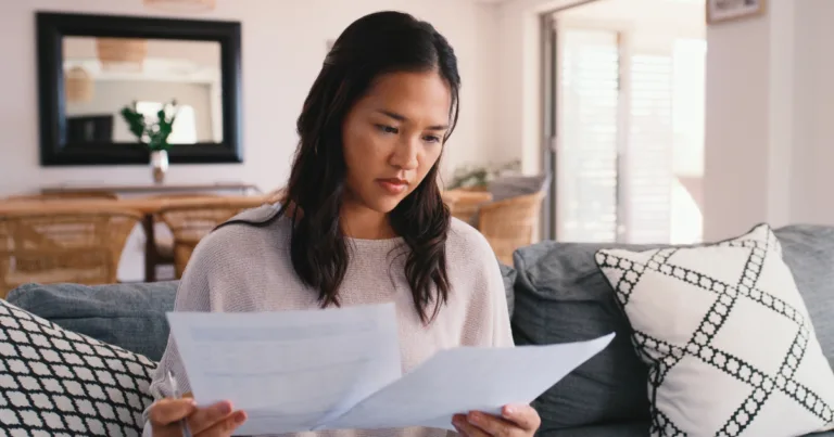 A woman reviews financial paperwork at home, weighing which bills to cut as other costs rise.