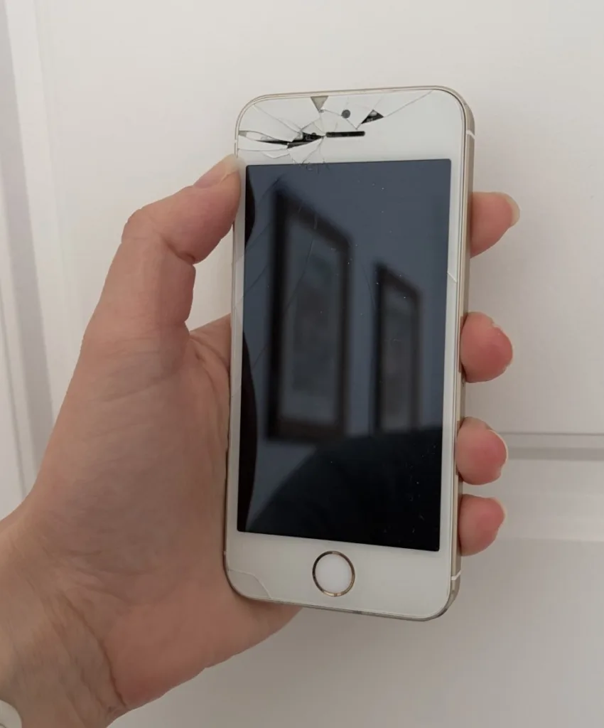 The reviewer’s hand holding her first smartphone, a broken iPhone 5S in gold.