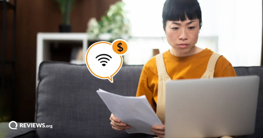 A woman frowns over a stack of bills and her laptop, weighing whether switching providers is worth the hassle to lower her monthly costs.
