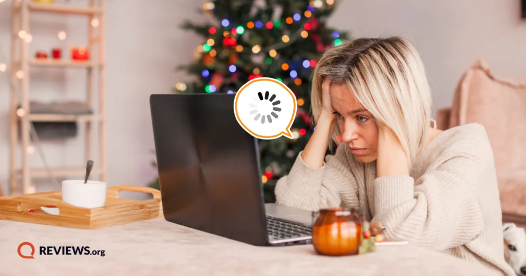 Woman stressed by a buffering laptop beside a lit Christmas tree, illustrating slow internet during holiday peak traffic.
