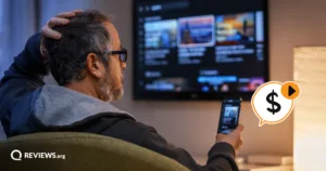 Man scratching his head while looking at his phone in front of a streaming menu, unsure whether to pay to share a family Hulu account.